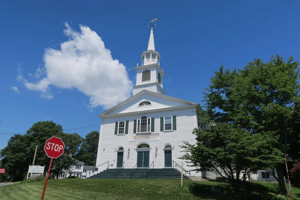The white First Parish meeting house in Westwood, with a tall steeple against a blue sky